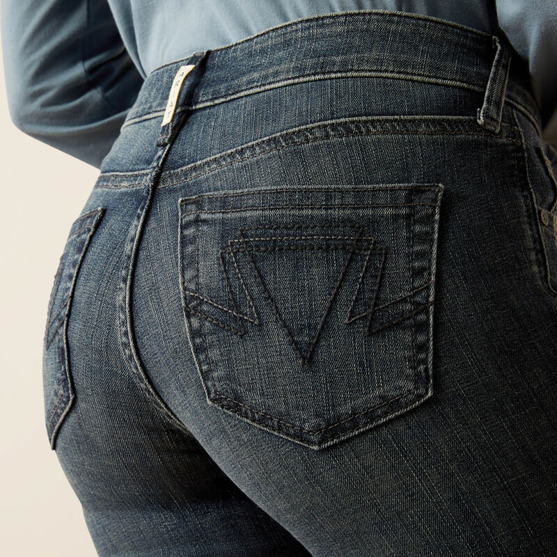 Close-up of dark blue jeans with a brand logo on the back pocket against a neutral background